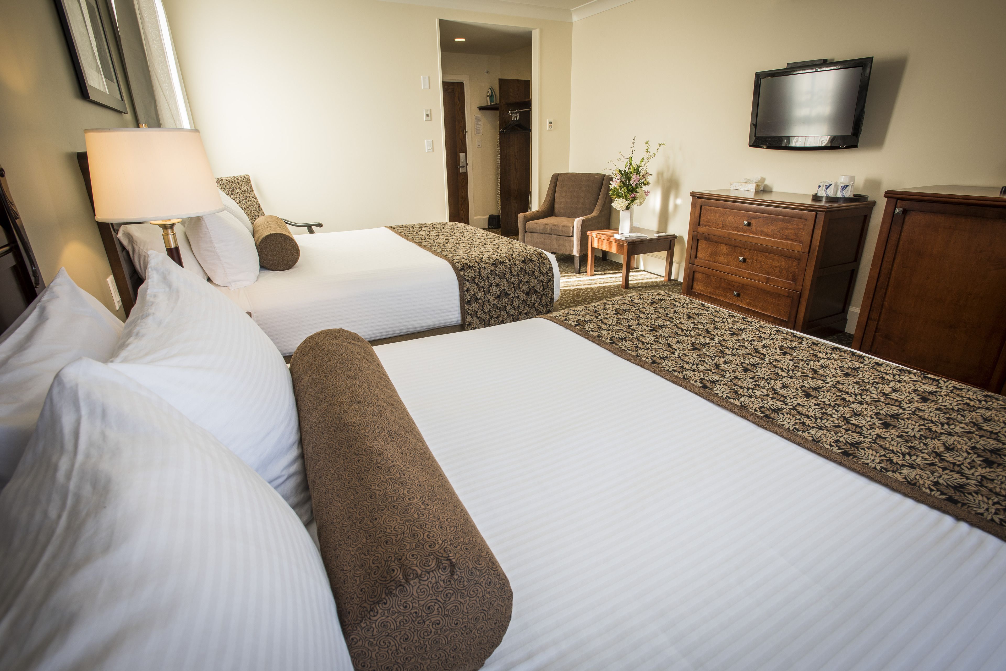 A hotel room with two beds, a desk, a chair, a television, and a wardrobe.