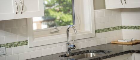 A kitchen with white cabinets, a stainless steel sink, and a window with a view of greenery outside.
