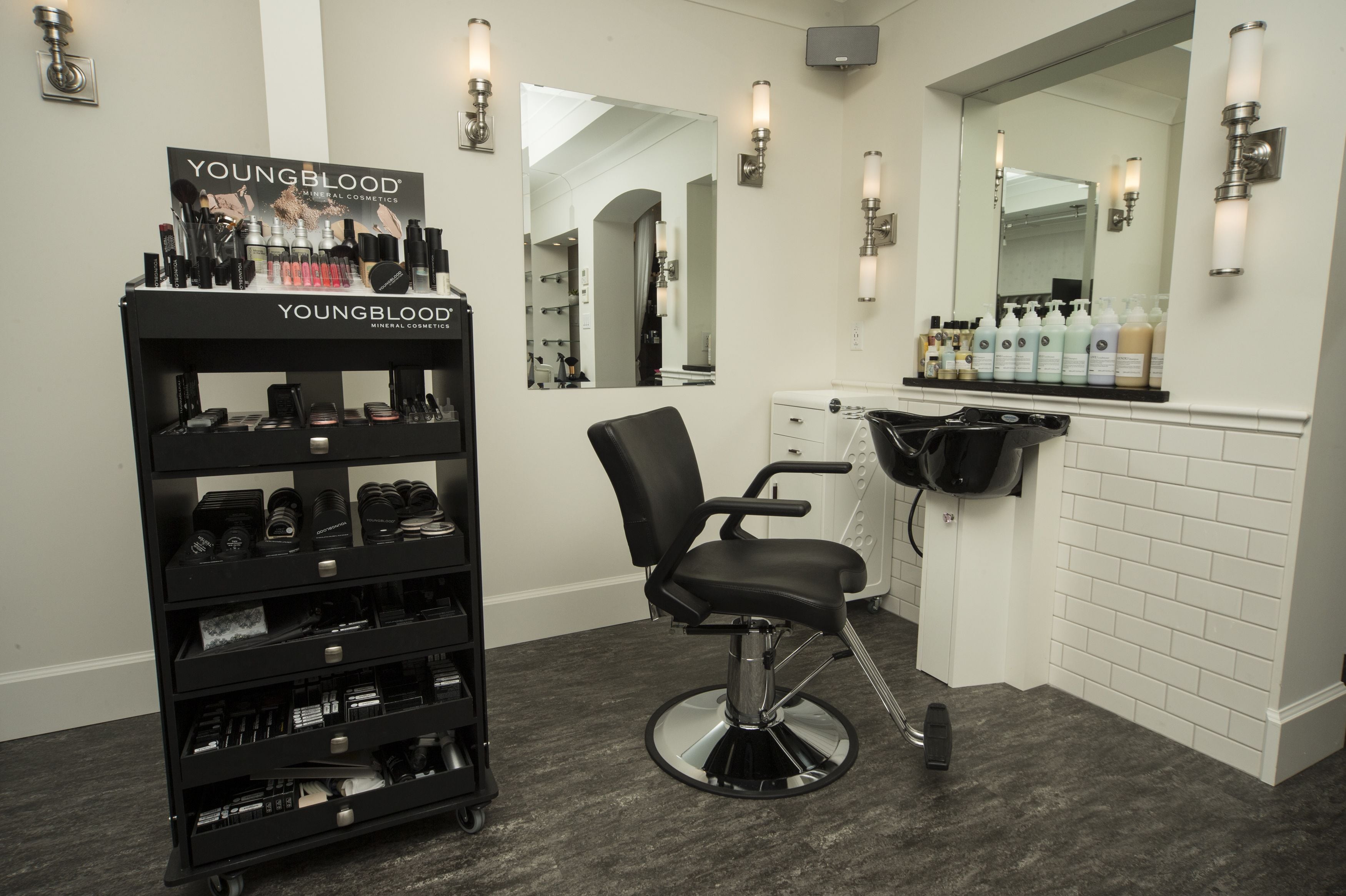 Un salon de beauté avec un fauteuil noir, un présentoir de produits de maquillage minéraux de la marque Youngblood et un miroir au-dessus du comptoir.
