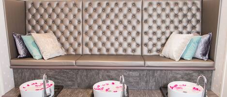 A bathroom with a tufted bench, three sinks with rose petals, and wall-mounted lights.