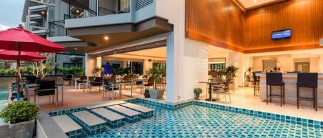 A modern hotel with a pool area, outdoor seating, and a bar.