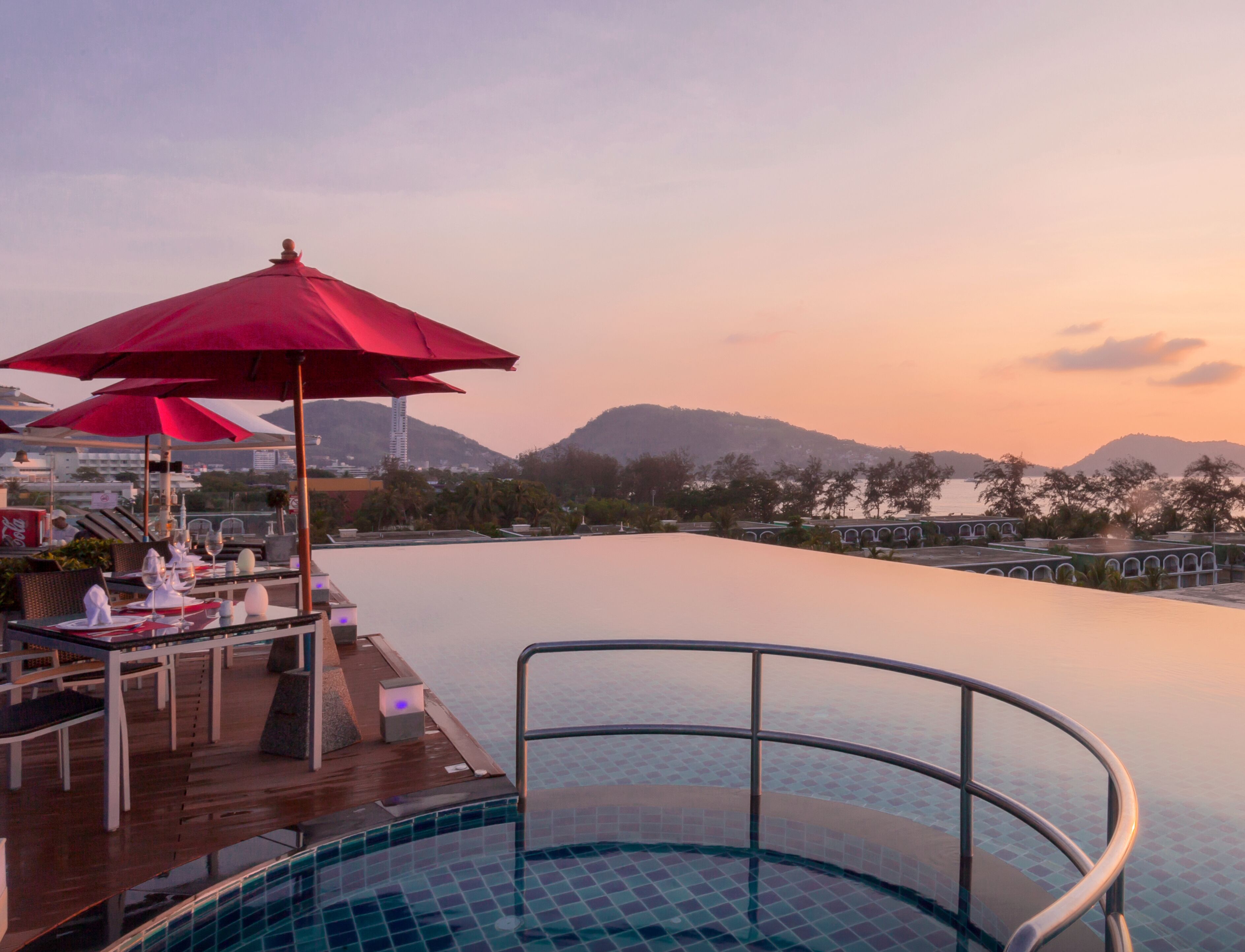Uma área de piscina no terraço, com guarda-sóis vermelhos e vista para as montanhas ao fundo.