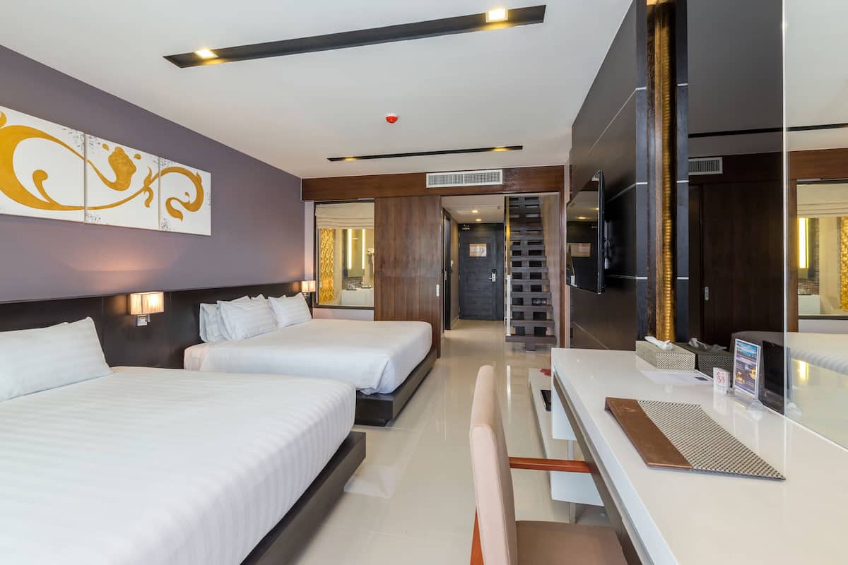 A hotel room with two beds, a desk, a chair, a TV, and a large mirror.
