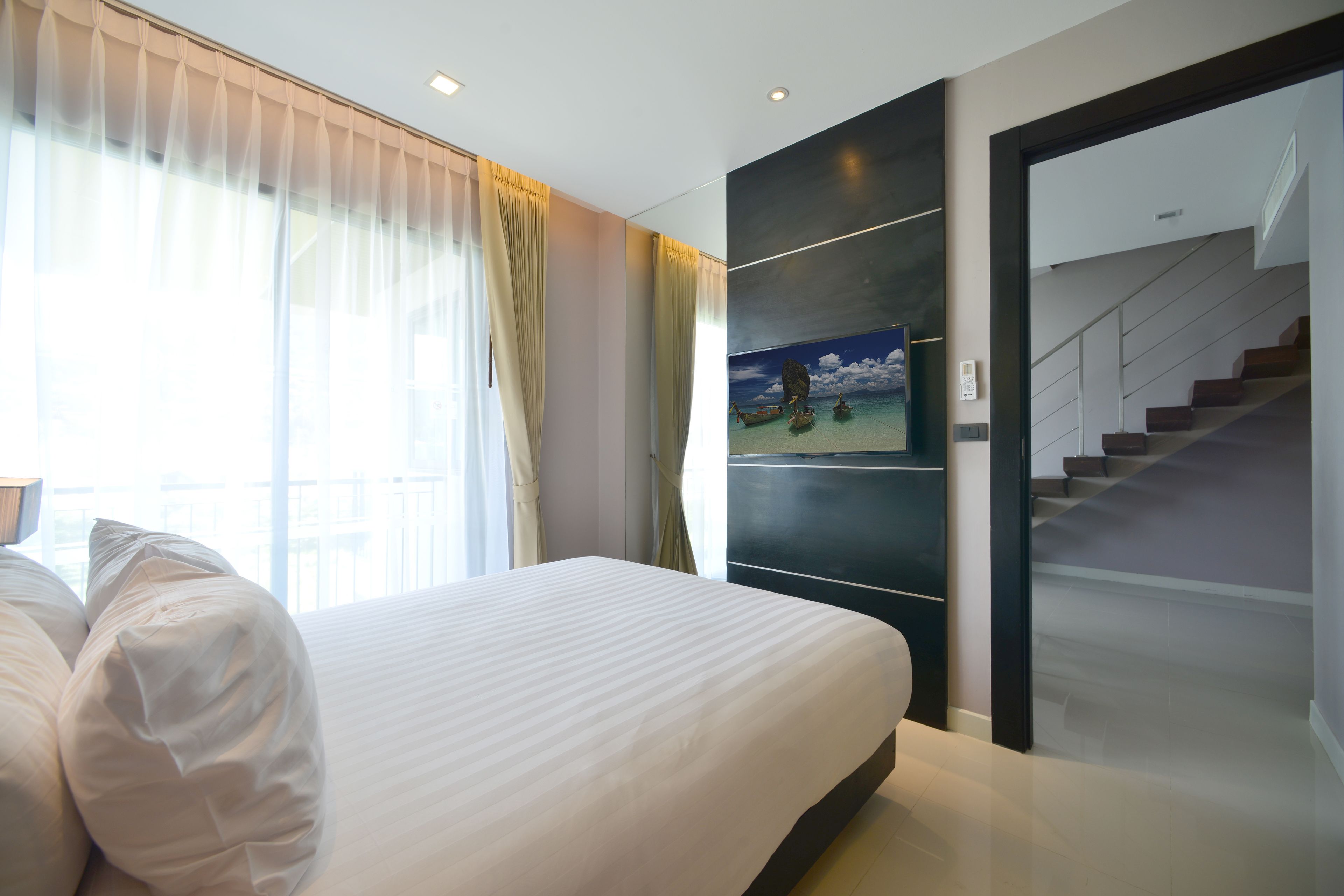 A modern hotel room with a large bed, a painting of a tropical scene, and a staircase leading to an upper floor.