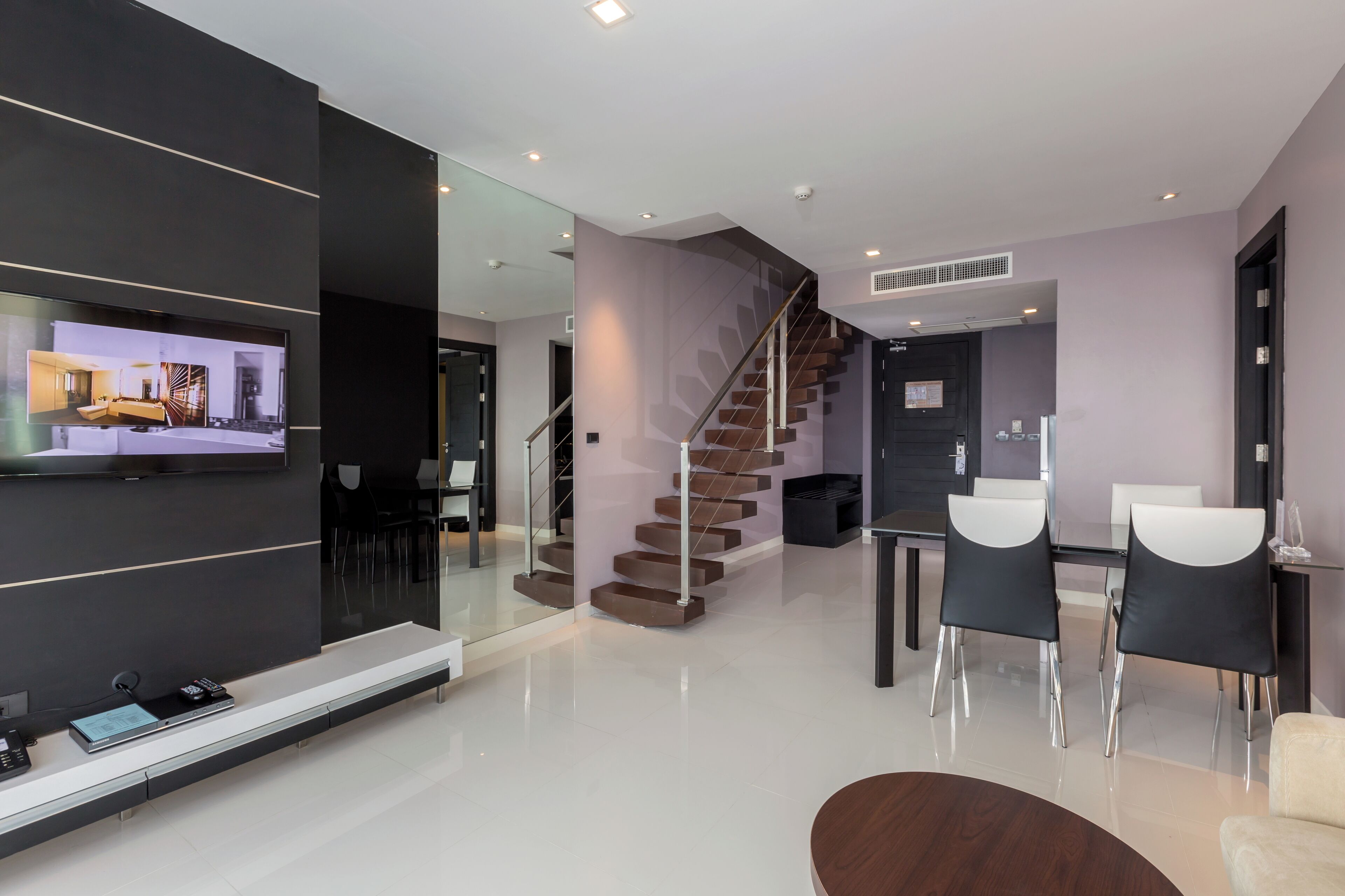 A modern living room with a flat-screen TV, a staircase, and a dining area with chairs and a table.