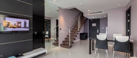 A modern living room with a flat-screen TV, a staircase, and a dining area with chairs and a table.