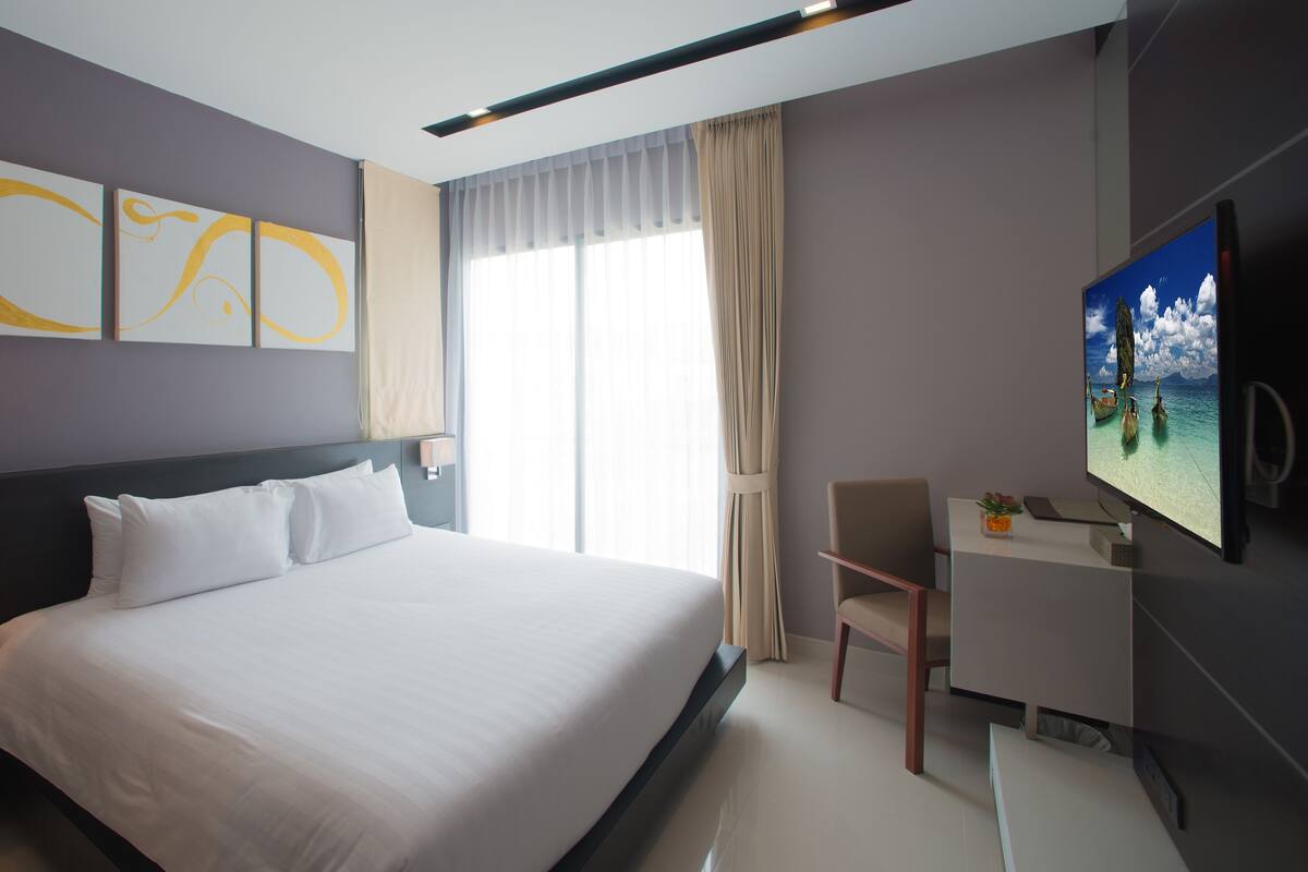 A hotel room with a large bed, a desk, a television, and artwork on the wall.