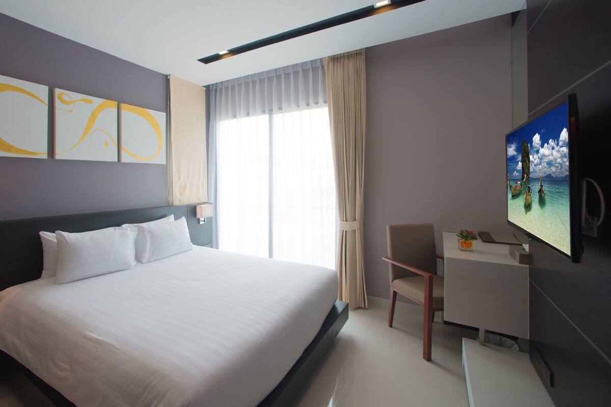 A hotel room with a bed, a desk, a chair, a TV, and a window with curtains.