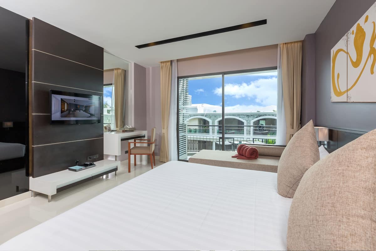 A modern hotel room with a large bed, a desk with a chair, a TV mounted on a wall, and a balcony with a view of the city.