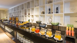 Zona de bufé con diversas opciones de comida y bebida, como frutas, jugos y salsas.