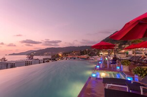 Zona de piscina con sombrillas rojas, sillas de descanso y vista al mar al anochecer.