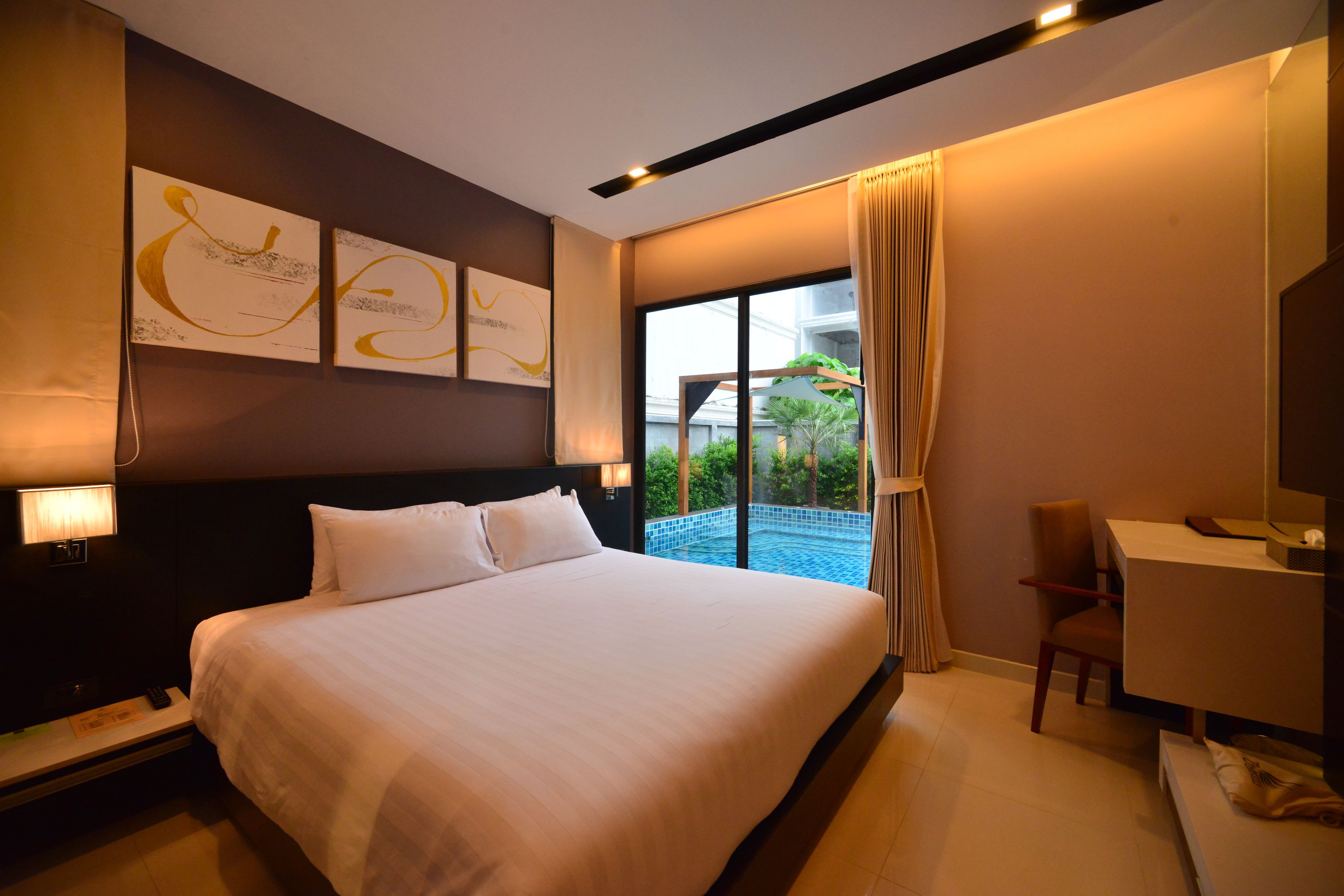 Ein Hotelzimmer mit einem großen Bett, einem Schreibtisch und Blick auf einen Swimmingpool.