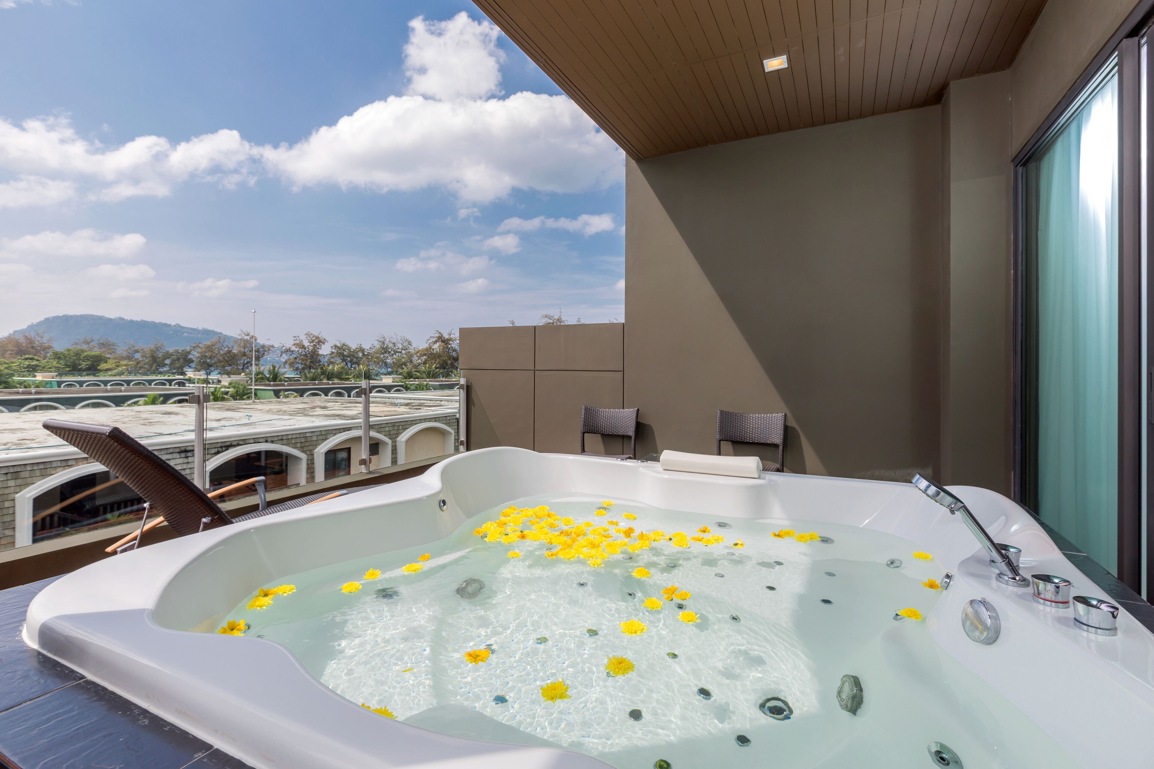 A modern bathroom with a large bathtub filled with water and yellow flowers, a shower area, and a view of a mountain.