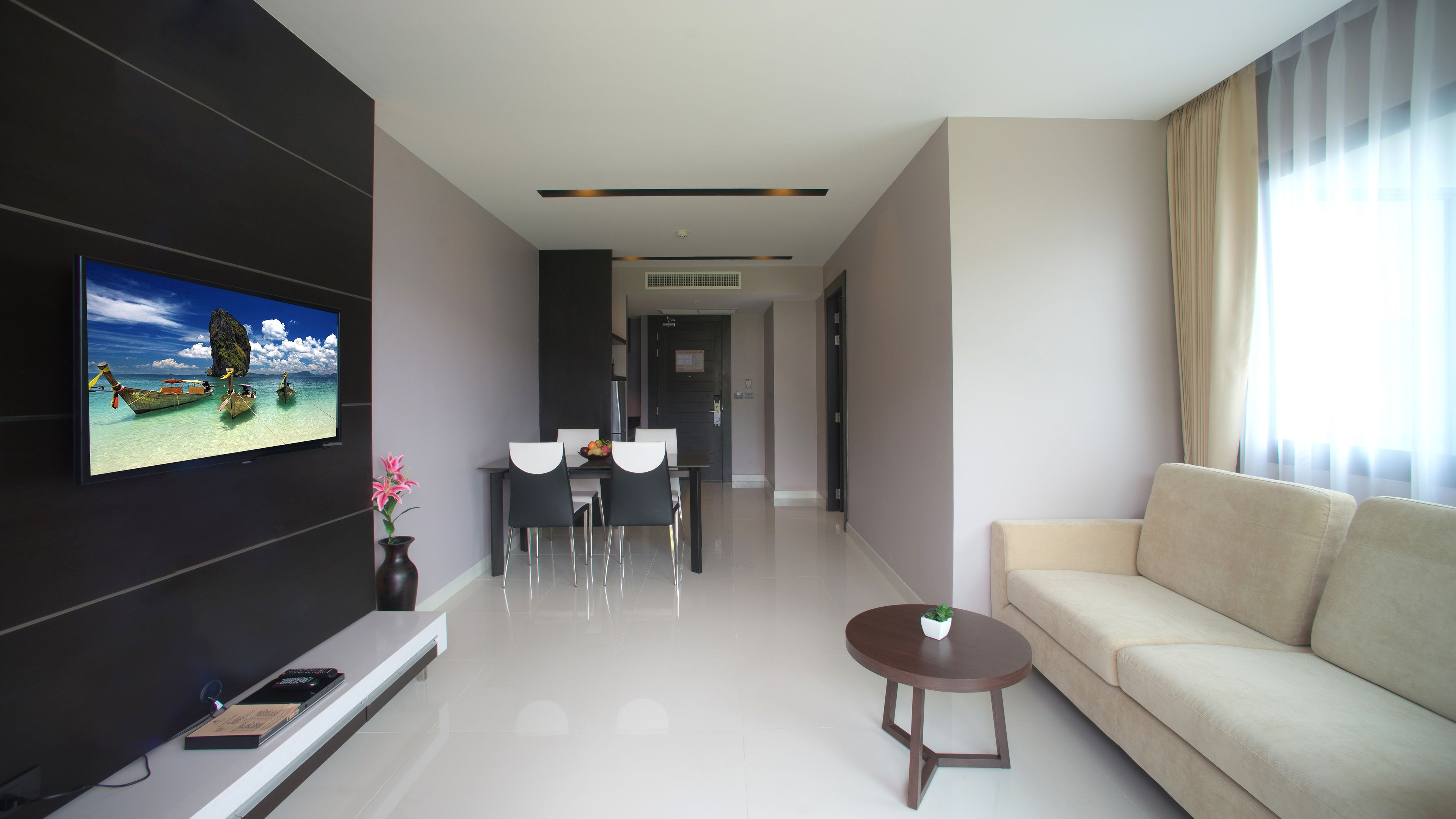 A modern living room with a flat-screen TV, a sofa, a dining area with chairs, and a coffee table.