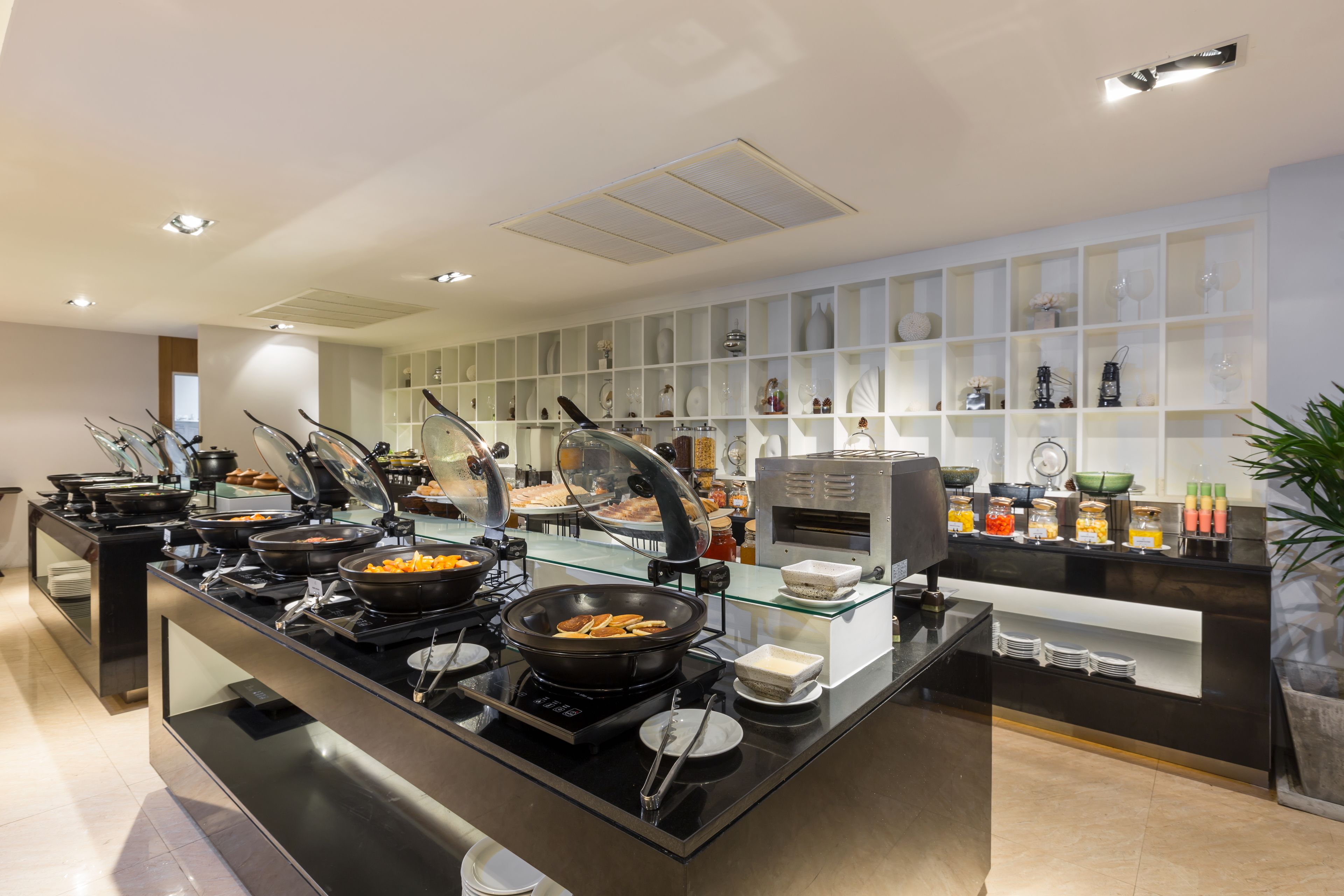 A buffet setup with various food stations, a coffee machine, and a display of glassware.