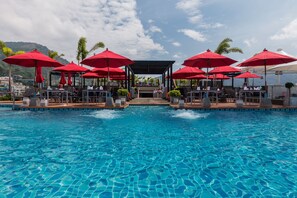 Un espace aménagé au bord de la piscine, avec des parasols rouges, des chaises longues et une vue sur l’océan.