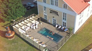 An outdoor swimming pool area with lounge chairs and a wooden deck, surrounded by a building with a sign reading "Skansen Hotel." - Hotel Skansen (Farjestaden)