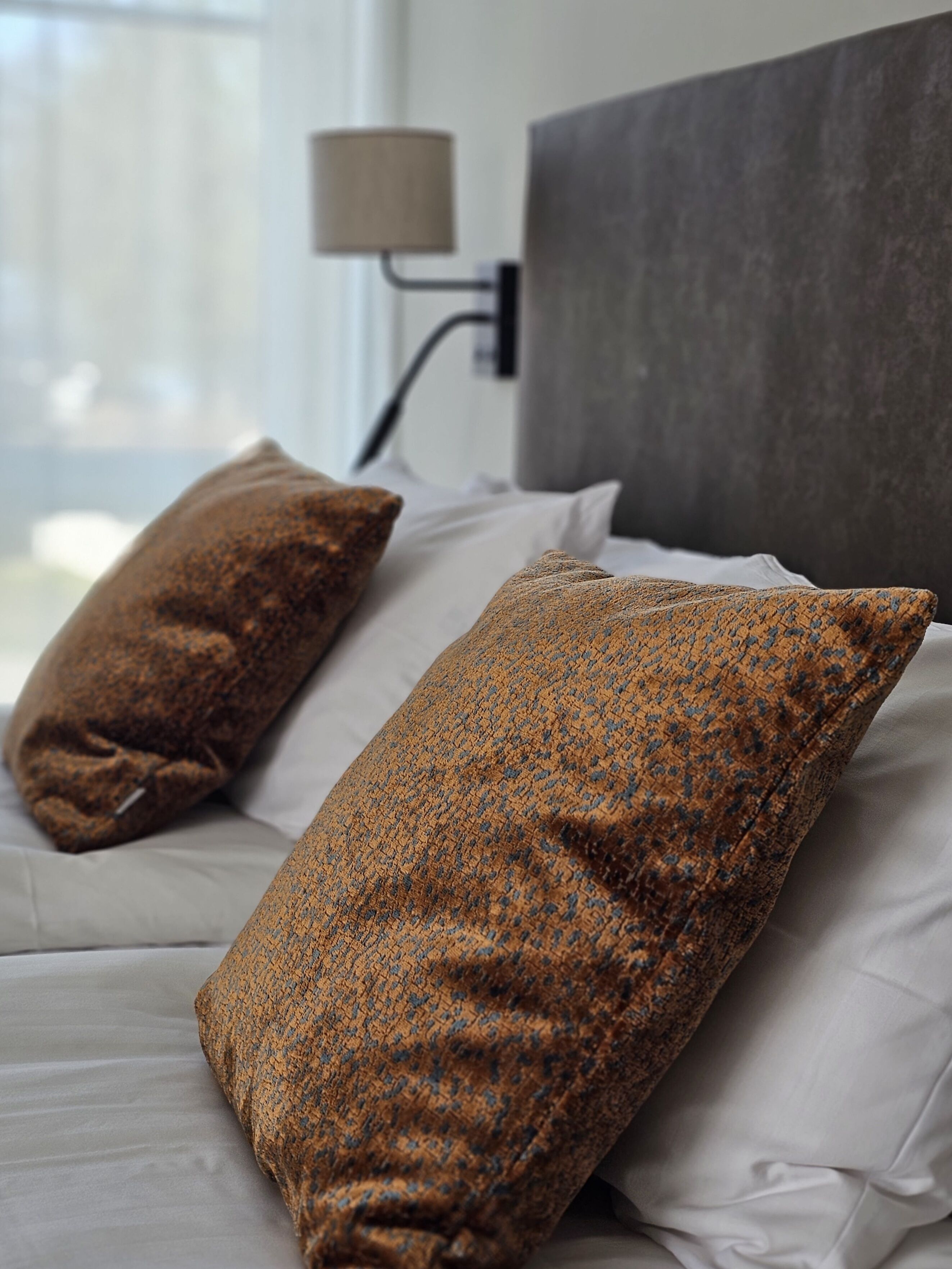 A bed with white linens and two brown pillows.