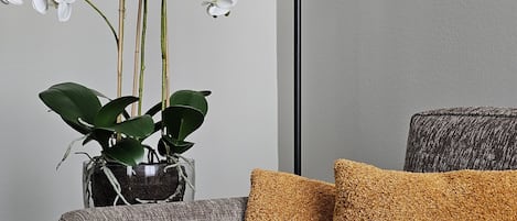 Un sofá gris con tela texturizada, una lámpara de pie negra y una planta en maceta con flores blancas.