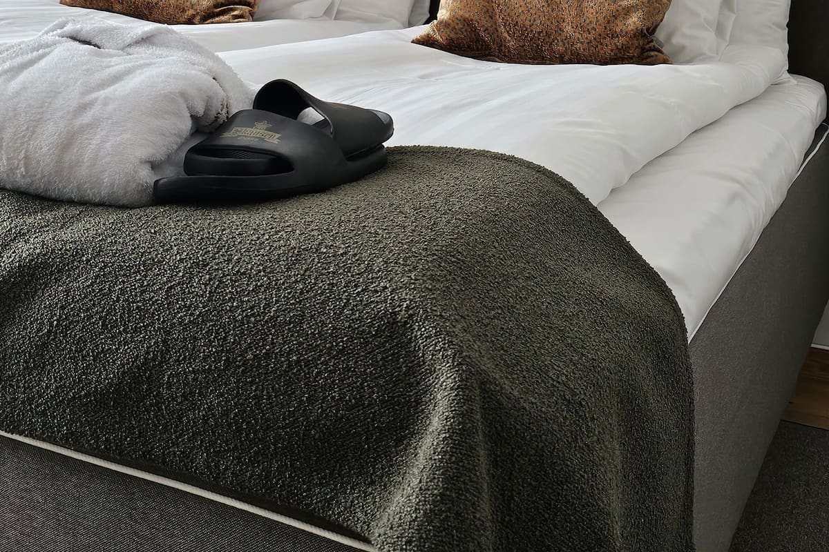 A neatly made bed with white linens, two brown patterned pillows, a grey headboard, and a black lamp on the nightstand.