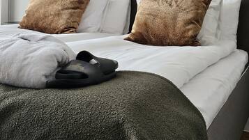 A neatly made bed with white linens, two brown patterned pillows, a grey headboard, and a black lamp on the nightstand.