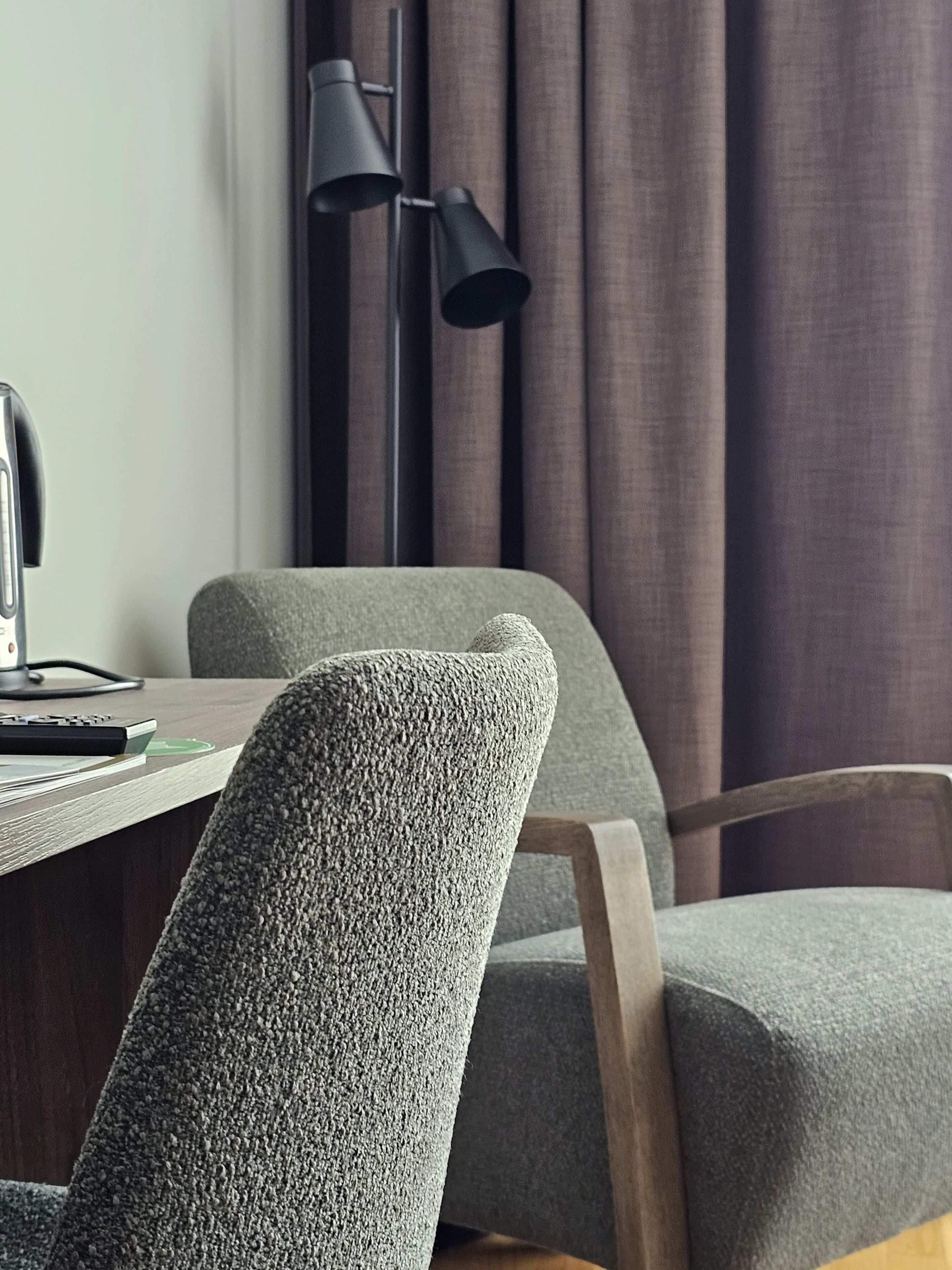 Una silla de oficina moderna con tela texturizada, un escritorio con computadora y teclado, y una lámpara de pie negra.
