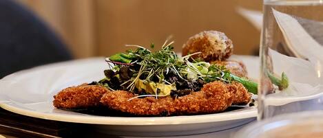 A plate of food with a breaded item, greens, and a small round item, on a white plate.