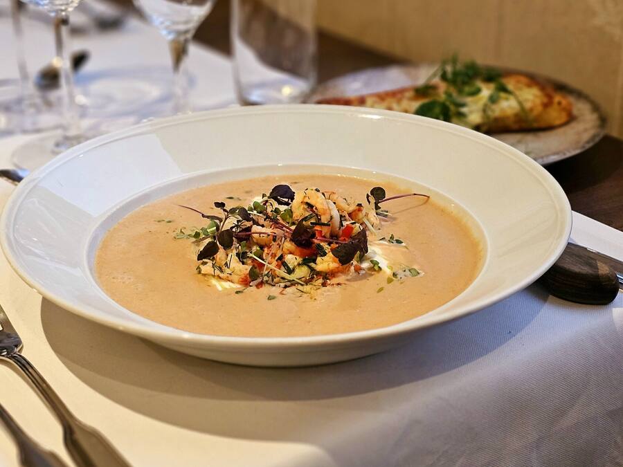 Eine Schüssel Suppe mit einer Garnitur auf einem weißen Teller, platziert auf einem Tisch neben einem Messer und einer Gabel.