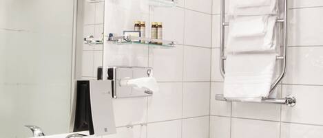 A modern bathroom with a white sink, a glass shelf with toiletries, a towel rack, and a mirror.