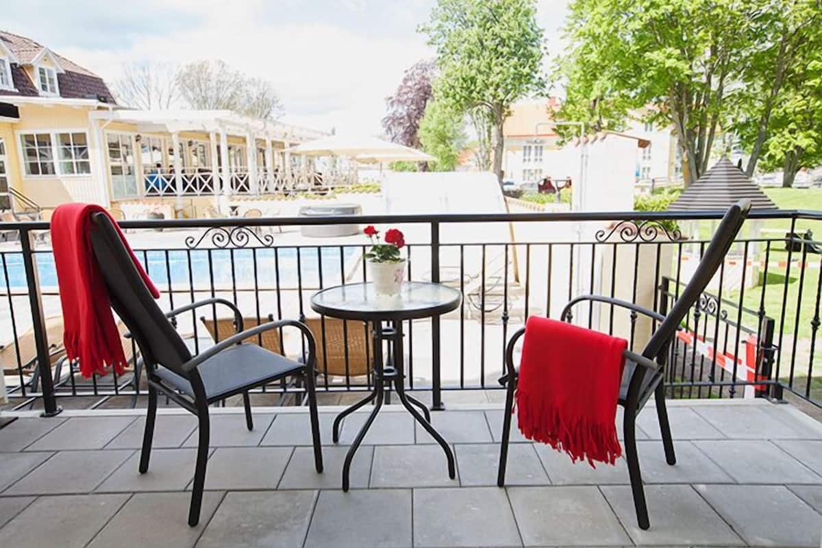 A balcony with two chairs and a small table, overlooking a pool area and a building with a white facade.