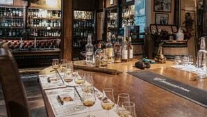 Una zona de bar con mostrador de madera, botellas, vasos y un sofá de cuero.