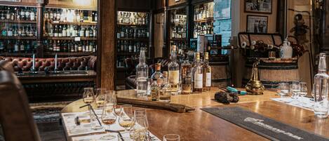 A bar area with a wooden counter, bottles, glasses, and a leather couch.