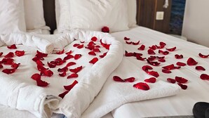 Una cama impecable con sábanas blancas y pétalos de rosa roja esparcidos sobre ella.
