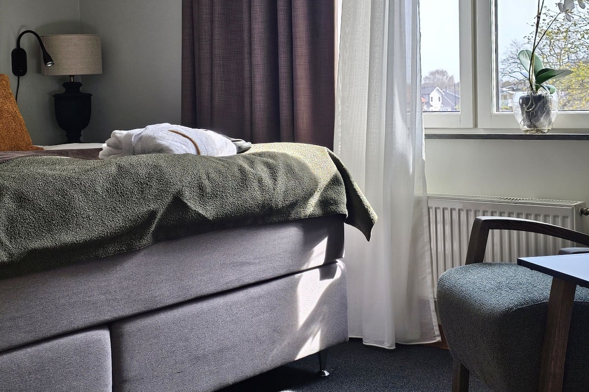 A modern bedroom with a bed, a bedside lamp, a window with curtains, and a view of the outside.