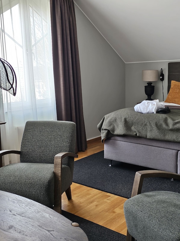 Una habitación de hotel con cama, dos sillones, una lámpara y una ventana con cortinas.