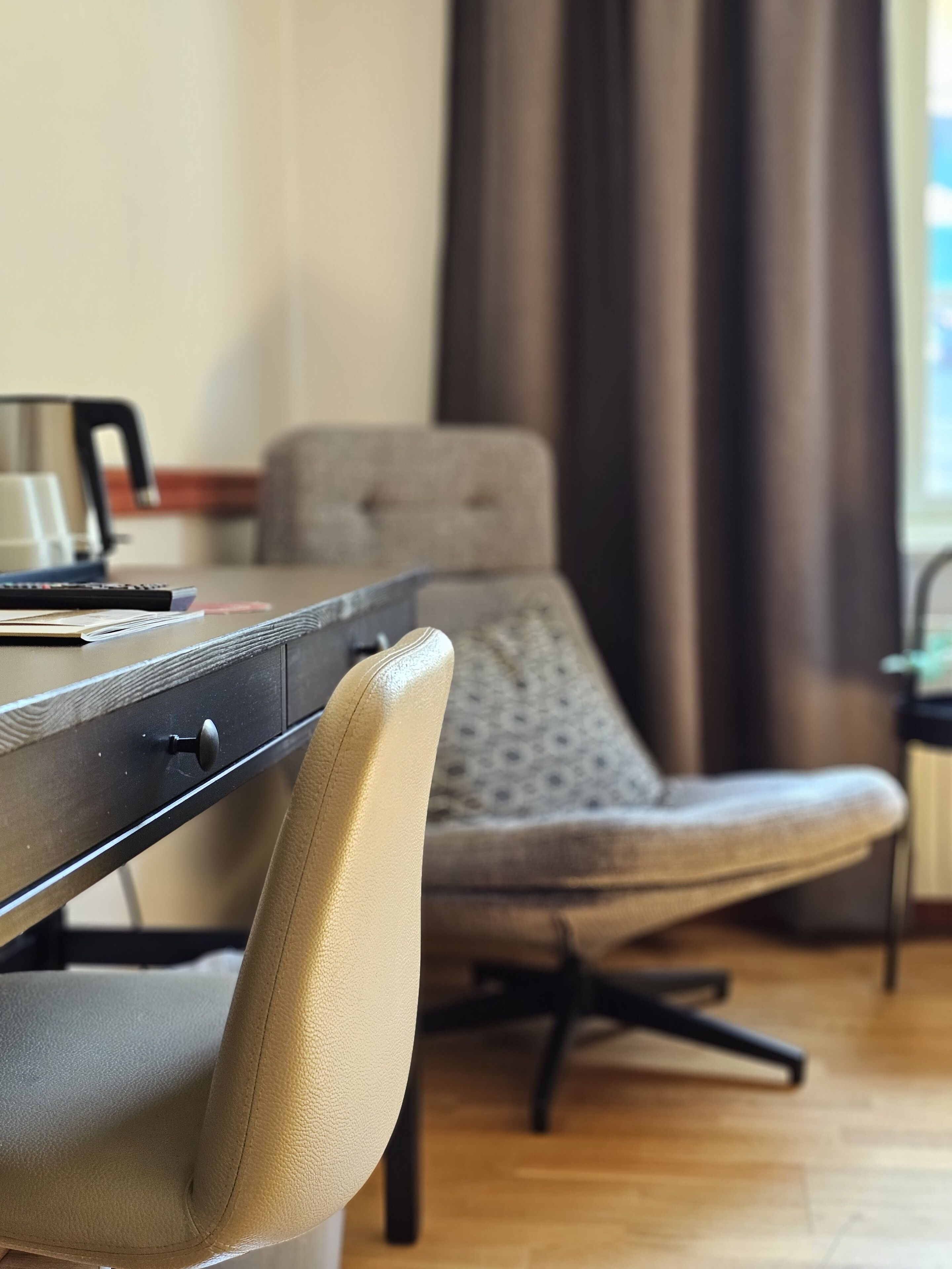 Una habitación con escritorio de madera, una silla, ventana con cortinas y un radiador.