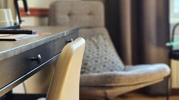 Ein Zimmer mit einem Holztisch, einem Stuhl, einem Fenster mit Vorhängen und einer Heizung.