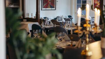 A restaurant with tables set for dining, a wine rack, and a painting on the wall.