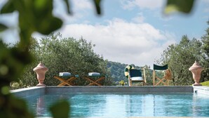 A pool area with lounge chairs and a flag, surrounded by greenery and trees.