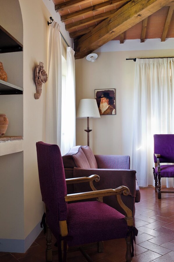 A room with a wooden ceiling, a sofa, a chair, a lamp, and a painting on the wall. - Casa Villa Rentals by Torre a Cona (Rignano sull'Arno)
