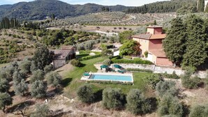 A villa with a swimming pool, surrounded by olive groves and hills.