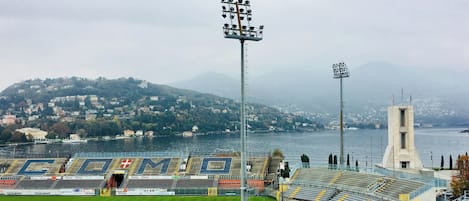 Un estadio con gradas vacías, un potente foco y vista a un lago con edificios al fondo.