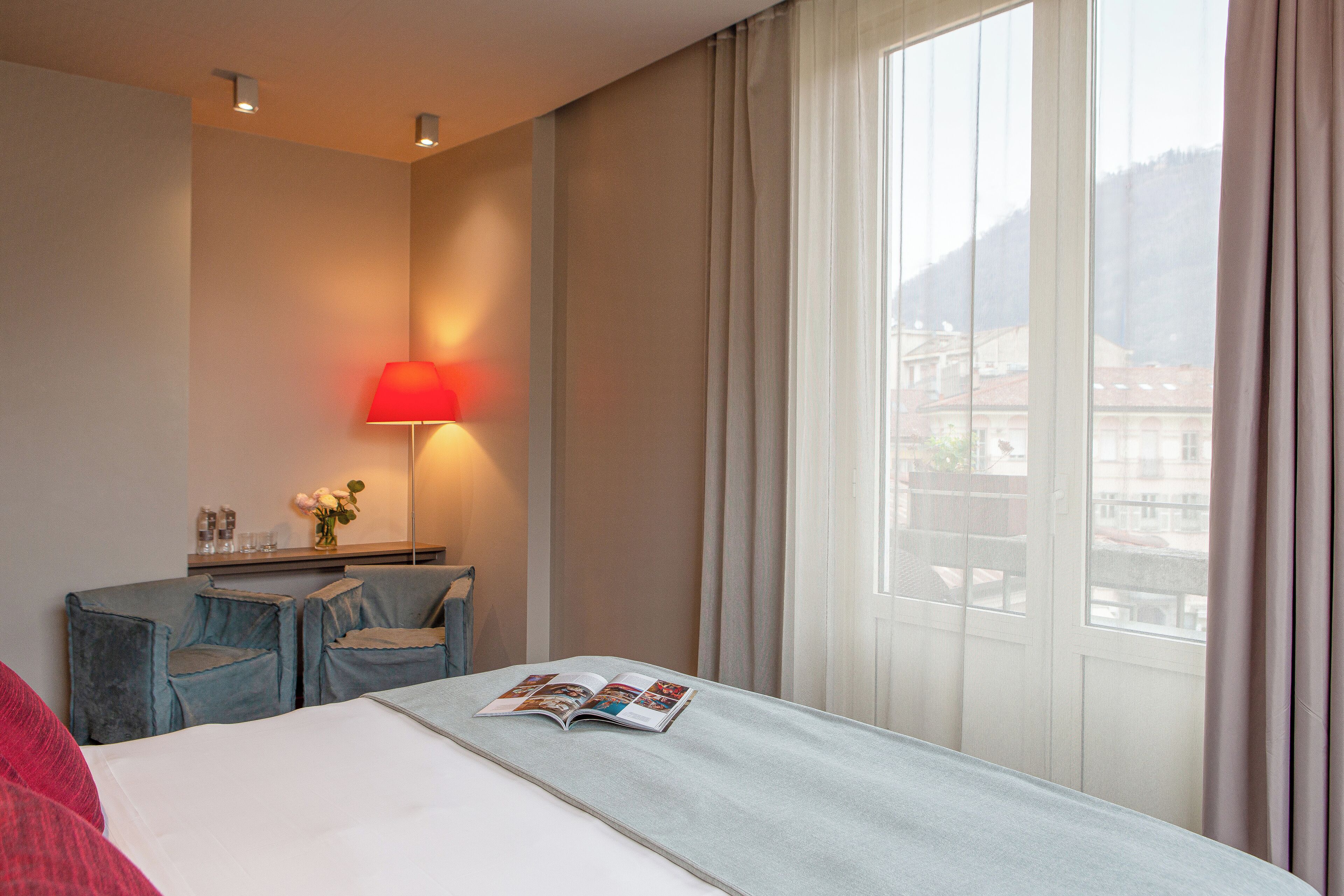 A hotel room with a bed, a desk, a lamp, and a window with curtains.