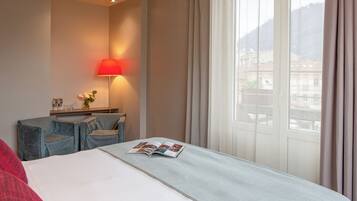 Ein Hotelzimmer mit Bett, Schreibtisch, Lampe und einem Fenster mit Vorhängen.