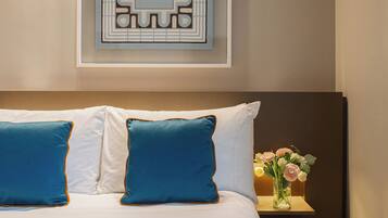 Una cama bien hecha con almohadillas azules y blancas, un adorno en la pared y una mesita de noche con un florero.