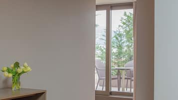 A room with a wooden floor, a small table with a vase of flowers, and a view of an outdoor balcony with chairs.