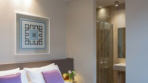 A hotel room with a bed, a nightstand with a vase of flowers, a bathroom with a glass shower, and a framed artwork on the wall. - Posta Design Hotel (Como)