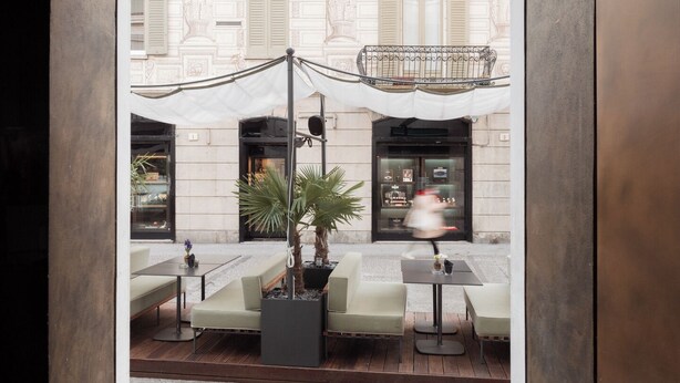 An outdoor seating area with tables and chairs, a potted plant, and a lamp. - Posta Design Hotel (Como)