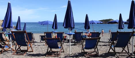 Een privéstrand, ligstoelen aan het strand, parasols, windsurfen