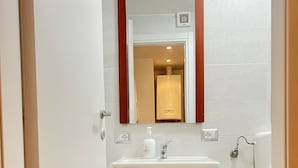 Une salle de bain avec un meuble-lavabo blanc, un miroir avec un cadre en bois, des toilettes et un espace douche.